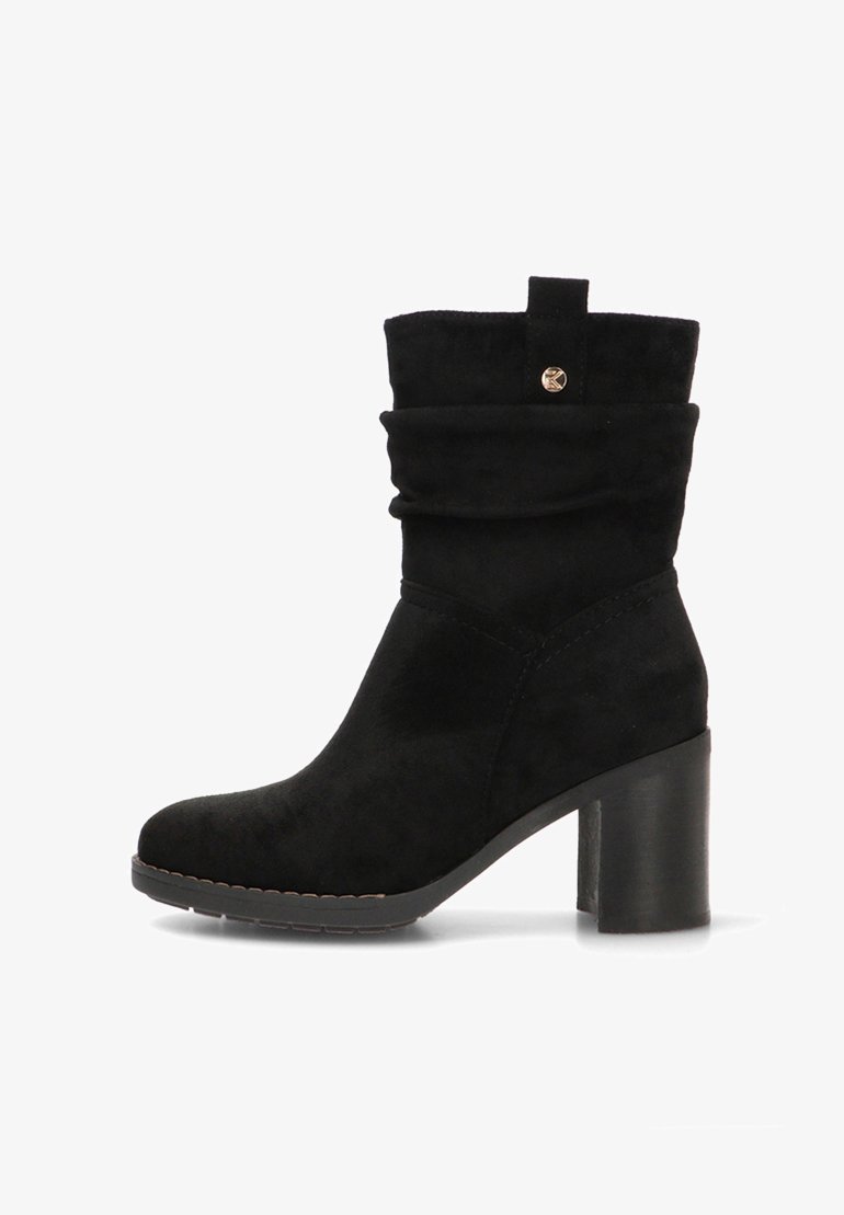 Botín de ante negro con una parte superior caída, punta redonda y tacón grueso. Presenta un pequeño botón dorado como acento y detalles de costura.