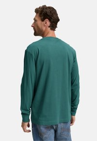 Camicia a maniche lunghe in cotone verde scuro, con una vestibilità rilassata e scollatura rotonda. Texture liscia, design minimalista e senza motivi visibili.