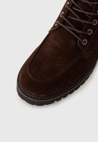 Bruna mockaskinnsankle boots med rund tå, snörning fram och texturerad gummisula med sömnadsdetalj längs kanten.