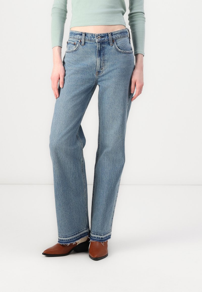 Jean en denim léger taille haute de couleur bleu clair, avec une coupe relaxée, présentant des décolorations subtiles, un ourlet brut, et un design classique à cinq poches.