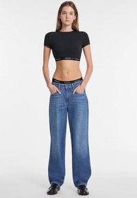 T-shirt nera cropped con maniche corte, abbinata a jeans a gamba larga in denim blu chiaro con vita alta e design a cinque tasche standard.