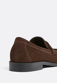 Braune Wildleder-Lederhosen mit niedrigem schwarzen Gummihaken und Stichdetails an der Seite, mit einem offenen Design oben.
