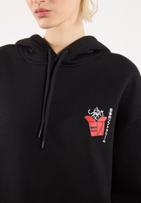 Black hoodie with a large front pocket, drawstrings, and a graphic of a red takeout box with noodles and text design on the chest.