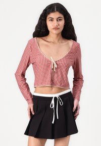 Red and white gingham crop top with long sleeves and lace trim, paired with a black pleated skirt featuring a white drawstring waistband.