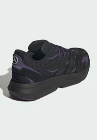 Black athletic shoe with mesh detailing and purple accents, featuring a thick sole and lacing system, branded with a silver logo on the heel.
