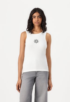 White sleeveless tank top with a ribbed texture, featuring a black sun graphic centered on the chest. Paired with light gray wide-leg jeans.