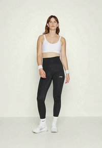 Top bianco sportivo e leggings neri a vita alta con un motivo sottile. Completati da sneakers bianche e polsini. Design semplice e funzionale.