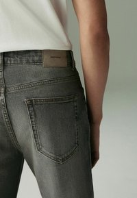 Szare dżinsy wykonane z denimu, o dopasowanym kroju, z skórzaną naszywką oznaczoną "DENIM SUPPLY" na tylnej części pasa oraz dwoma standardowymi tylnymi kieszeniami.