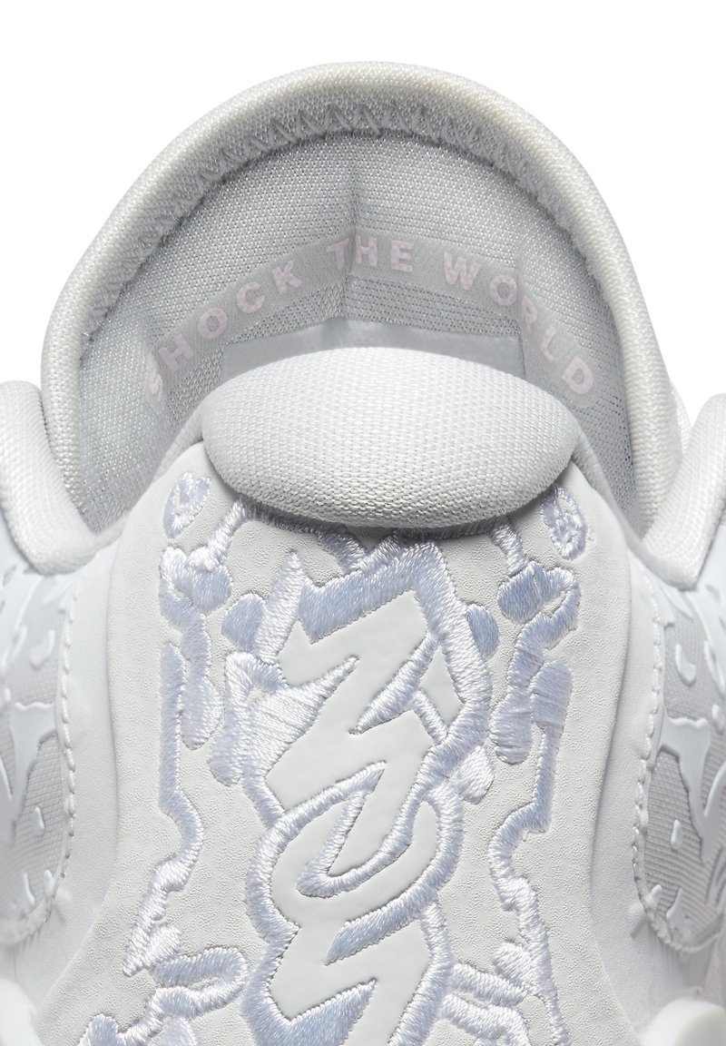 Talons de sneaker blancs avec broderie en forme d'éclair texturée et texte sur le col intérieur disant "SHOCK THE WORLD" en rose clair.