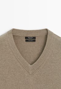 Beige Kaschmirpullover mit V-Ausschnitt und geripptem Kragen. Das Etikett trägt die Aufschriften "Massimo Dutti" und "100% Kaschmir." Weiche Textur.