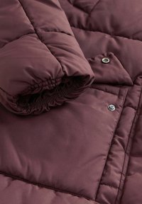 Bordeaux gewatteerde jacket met een gequilt ontwerp, elastische manchet en drukknoopdetail. Gladde stof met een lichte glans.