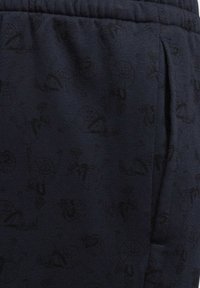 Schwarze Jogginghosen aus strukturiertem Stoff mit einem dezenten Muster in hellgrauen Designs und einer Seitentasche sowie einem elastischen Bund.