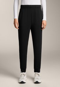 Čierne atletické joggery s elastickým pásom, úzkym strihom a zúženými členkami. Nosené s svetlými teniskami.