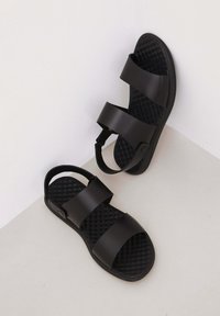 Czarne sandały z dwoma szerokimi paskami, teksturowaną wkładką oraz regulowanym paskiem piętowym; wykonane z materiału syntetycznego dla zwiększenia trwałości.