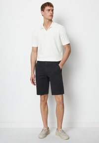 Herrklädsel som består av en ljusfärgad kortärmad polo och mörka shorts. Shortsen har fickor, och han bär ljusfärgade casual-skor.
