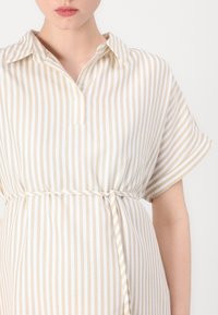 Abito a righe beige e bianche con maniche corte, colletto e un fiocco in vita. Tessuto leggero con una trama liscia.