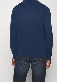 Navyblauer, strukturierten Strickpullover mit Rundhalsausschnitt und langen Ärmeln, kombiniert mit dunkelblauen Jeans mit Gesäßtaschen.