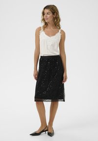 Camiseta de tirantes con encaje blanco y falda negra con lentejuelas. La falda es de longitud hasta la rodilla con una cinturilla suave, acompañada de tacones negros.