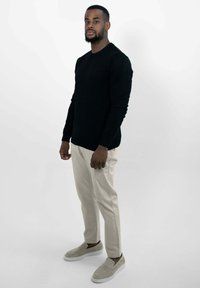 Zwarte langefsleevetrui, crèmekleurige broek en grijze instapschoenen. Lichtgewicht textuur, aansluitend ontwerp, effen patroon zonder opvallende accenten.