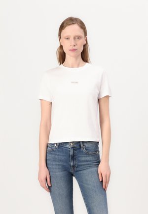 Bijela pamučna majica s okruglim izrezom i kratkim rukavima. Ima mali, centrirani Calvin Klein logo u suptilnom fontu.