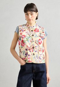Blommig quiltad väst i krämfärg med livfulla röda, blå och gröna mönster; har två framfickor, rund halsringning och knäppning.