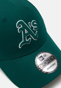 Πράσινο καπέλο του μπέιζμπολ φτιαγμένο από ύφασμα με κεντημένα λευκά γράμματα "A's" και ασημένια αυτοκόλλητη ρυθμιστική ετικέτα στο χείλος.