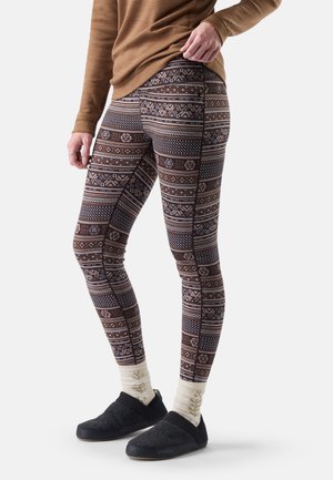 Persona con mallas marrones estampadas, calcetines crema con diseño de hoja, zapatos negros sin cordones y una camiseta marrón de manga larga sobre un fondo claro.