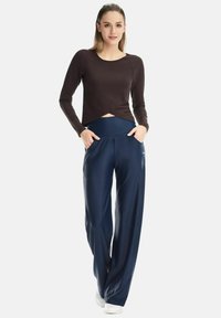 Long-sleeve brown top with a cropped design and round neckline paired with navy high-waisted pants featuring pockets and a smooth texture.