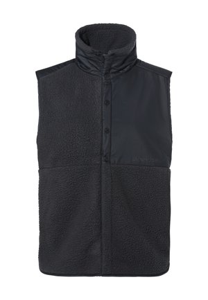 Schwarze Weste mit hohem Kragen, die eine Kombination aus glatten und strukturierten Materialien zeigt. Vorderknöpfe und Markenzeichen an der unteren Seite.