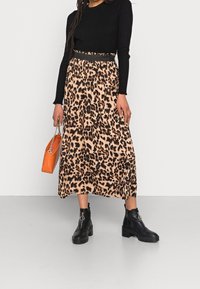 Leopardenmuster-Midi-Rock in Beige und Schwarz, aus glattem Stoff, kombiniert mit einem eng anliegenden schwarzen Rippenpullover und klobigen schwarzen Stiefeln.