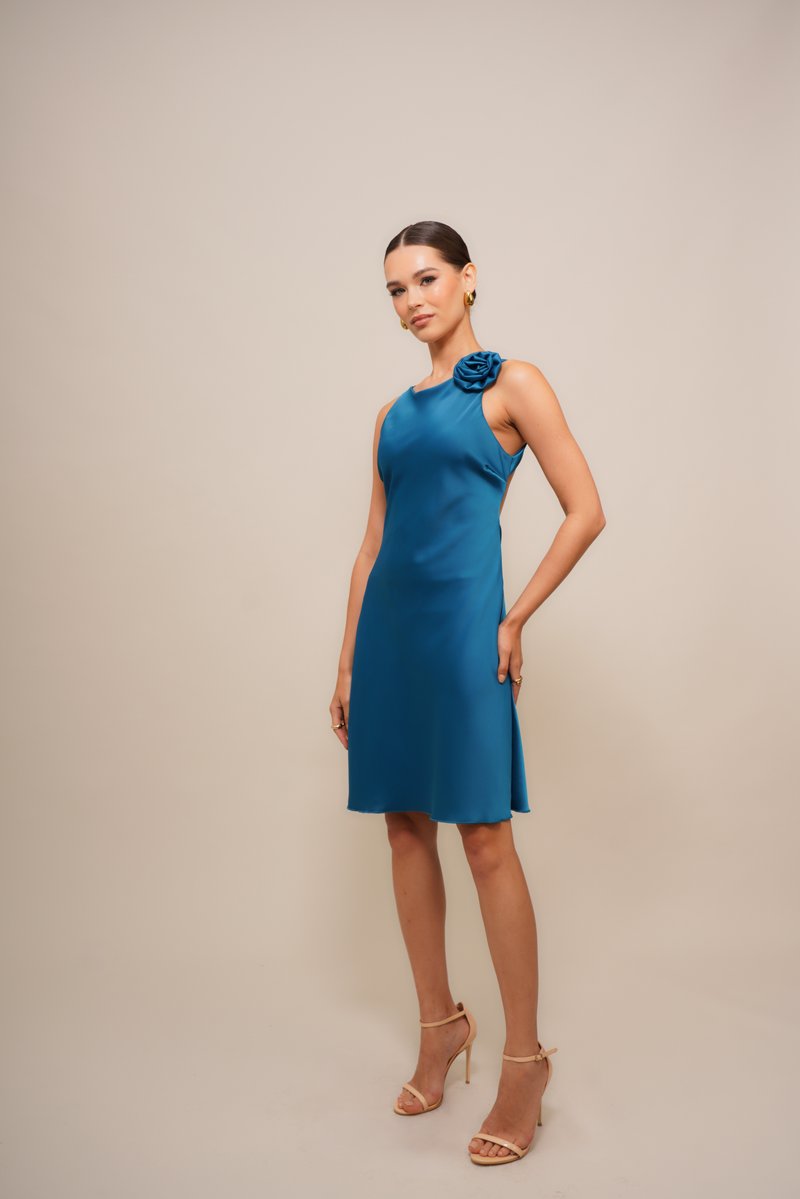 Teal satengkjole med tettsittende bodice, ermeløs design og blomsterdekorasjon på venstre skulder, knelengde med lett utforming.