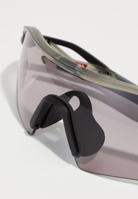 Okulary przeciwsłoneczne Oakley z przejrzystą, szaro-srebrną oprawką, ciemnymi soczewkami i gumowym noskiem. Ich sportowy design charakteryzuje się zaokrąglonymi krawędziami oraz detalami z logo.
