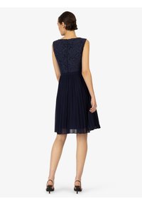 Robe bleu marine avec un corsage en dentelle, jupe plissée et sans manches. Fermeture éclaire au dos et quincaillerie minimale. Texture lisse.