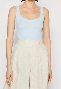 Débardeur bleu clair côtelé avec un col en V, associé à un pantalon beige taille haute avec des plis et une coupe ajustée. Texture lisse dans l'ensemble.