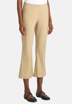 Donna che indossa pantaloni beige cropped a gamba larga abbinati a ballerine Mary Jane nere con dettagli fibbia argentata.