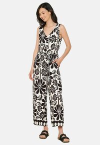 Črno-bela cvetna kombinezon z V-izrezom, širokimi hlačnicami in zavezanem pasu, s poudarjenim cvetličnim vzorcem in žepi. Rjave sandale za popoln videz.