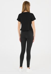 Schwarzes Crop-Top mit kurzen Ärmeln, kombiniert mit hochtaillierten schwarzen Leggings. Beide Kleidungsstücke haben eine glatte Textur. Sneakers runden das Outfit ab.