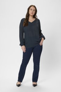 Mörkblå, långärmad blus med V-ringning och subtil textur. Serverad med blå denimjeans och svarta spetsiga klackar.