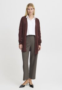 Burgundský cardigan s otevřeným předním dílem, nošený přes bílou košili s knoflíky; spárován se šedými kalhotami a černými lodičkami.