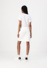 T-shirt en coton blanc associé à une jupe blanche longueur genoux, dotée d'une fente au dos et de poches avant en appliqué, portée avec des baskets blanches.