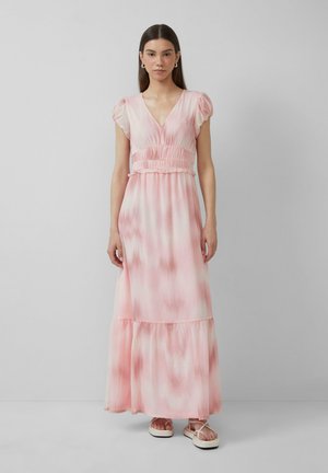 Longue robe rose avec un motif tie-dye, manches courtes à volants, taille smockée et jupe à niveaux. Portée avec des sandales de couleur claire.