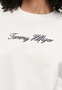 Biały sweatshirt z czarnym haftowanym napisem "Tommy Hilfiger". Okrągły dekolt i miękki materiał bawełniany oraz minimalistyczny design.