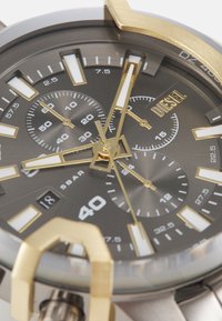 Orologio Diesel da uomo con quadrante grigio, dettagli dorati e indicatori bianchi delle ore. Presenta tre sottodial e una distintiva corona dorata.