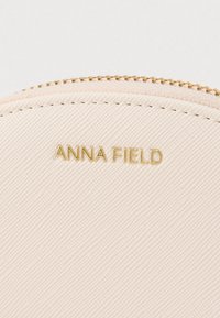 Trousse de maquillage rose clair avec surface texturée, fermeture éclair dorée et logo "ANNA FIELD" embossé à l'avant.