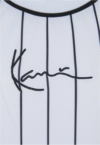 Hvid sportsjersey med sorte lodrette striber og en sort broderet signatur på brystet. Tekstureret, letvægtsstof.