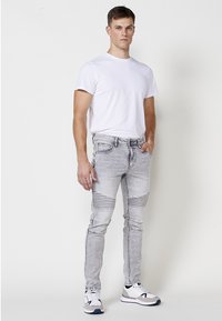 Herretøj bestående af en ensfarvet hvid t-shirt, lysegrå slidte skinny jeans med teksturerede knæakcenter, og atletiske sneakers i hvid og grå.