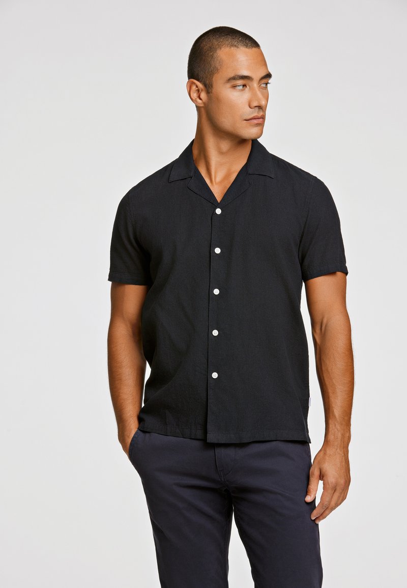 Μαύρο κοντομάνικο πουκάμισο με κουμπιά φτιαγμένο από υφασμάτινη υφή, με καμπυλωτό λαιμό και λευκά κουμπιά κατά μήκος της μπροστινής βελόνας.