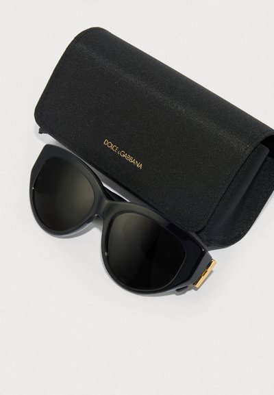 Óculos de sol oversized pretos com um acabamento brilhante, apresentando um detalhe dourado na têmpora. Inclui uma case de tecido preto com o selo "Dolce & Gabbana."