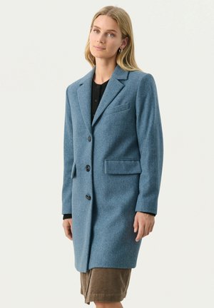 Cappotto in misto lana blu con un design sartoriale, caratterizzato da revers a punta, tre bottoni e due tasche frontali. Texture liscia e taglio moderno.