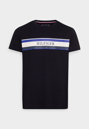 Camiseta de algodón negra con una amplia franja horizontal en blanco, azul y gris, con el nombre de la marca "HILFIGER" centrado en la franja.